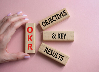 OKR objectives and key results symbol. Wooden blocks with words OKR objectives and key results. Businessman hand. Beautiful pink background. Business and OKR concept. Copy space.