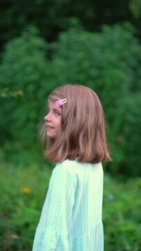 Mid-length portrait of a girl standing with her back to us, turning around and looking into the camera, vibrant green summer garden background, slow motion