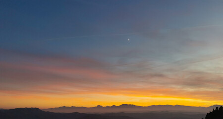 Fototapeta na wymiar Tramonto cobalto e arancio con luna nel cielo sopra le valli e le montagne