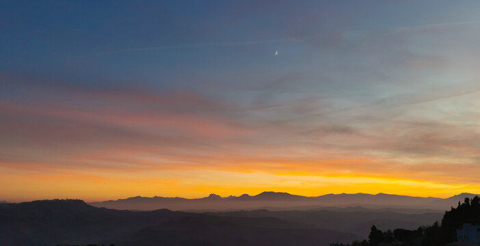 Tramonto cobalto e arancio con luna nel cielo sopra le valli e le montagne