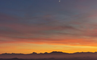 La Luna al tramonto nel cielo arancione sopra le montagne - obrazy, fototapety, plakaty