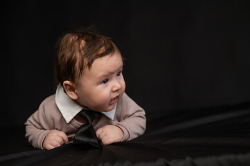 Portrait of a baby lying on his stomach wearing a tie on a black background.