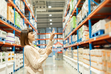 Warehouse worker hands holding tablet check stock on tall shelves in warehouse storage. Asian woman...