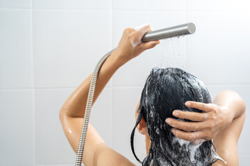 Young woman in shower rinse shampoo foaming with water dripping on hair and body. Taking shower relaxing under warm running water. Female washing her hair and hand to massage head while washing hair.