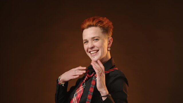 A vibrant lesbian with a spunky attitude and fiery red hair sports suspenders and a checkered tie, confidently posing against a deep brown background. Camera 8K RAW.