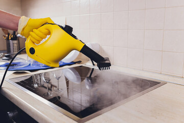 Cleaning kitchen hob with a steam cleaner.