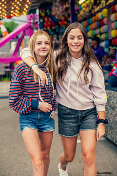 Candid photo of two cute and smiling teenage girls having fun at an outdoor carnival or theme park. Teenagers enjoying their free time together. Best friends hanging out at the carnival