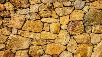 Sardinia, Italy - April 04, 2016 : A wall made of natural stones of many different sizes and shapes in yellow brown colors.