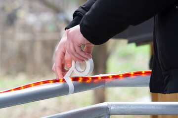 close up of a man taping Christmas string lights hose on a fence, hands decorating fence with christmas string lights close up, decorating at home