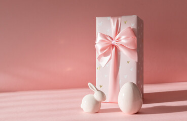 Porcelain Easter eggs and bunny with gift box on a pink background.