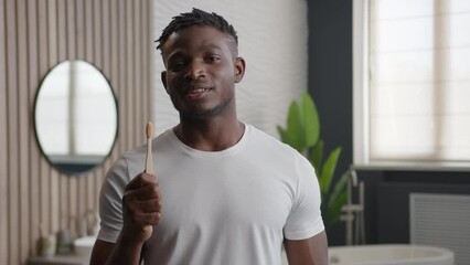 Young 30s African American man toothy smiling happy male guy model in bathroom holding brush toothbrush showing thumb up gesture recommend dental health care brushing teeth daily hygiene healthy smile