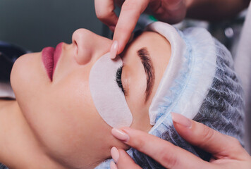 Eyelash Extension Procedure. Close up view of female eye with long eyelashes. Stylist holding pink...