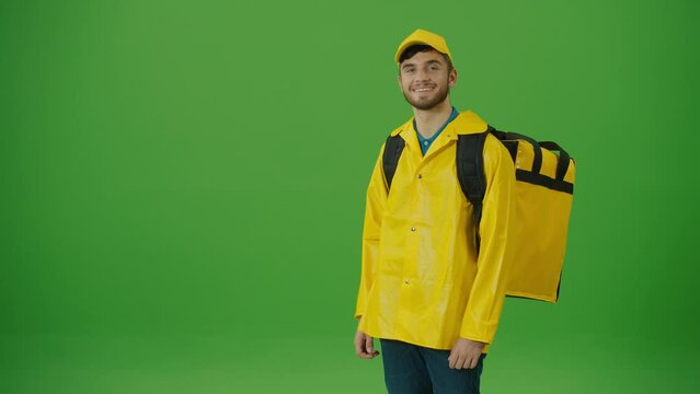 Green Screen Young Food Delivery Person in Yellow Uniform and With a Thermal Backpack and Using Smartphone to Check Order. Courier On the Way to Deliver Order to Client. Back View