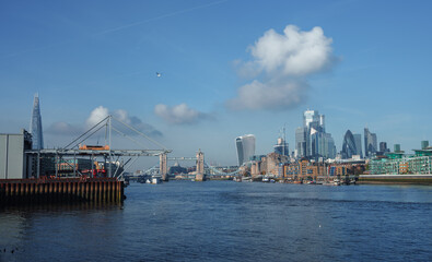Panoramic view of the River Thames with the London skyline, featuring the Shard, Tower Bridge, and modern skyscrapers under a clear blue sky. No signs of activity or holiday decor.