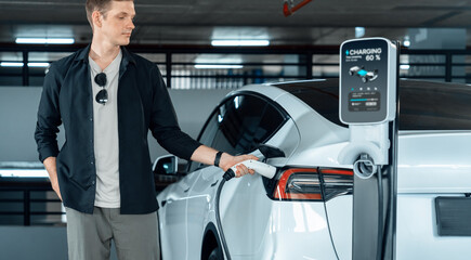 Young man travel with EV electric car to shopping center parking lot charging in downtown city...