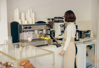 Back view of female barista grinding coffee using professional grinder machine in coffee house