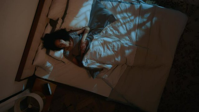 Disturbed African American girl woman sleep in bed night nap evening bedroom irritated female suffer night insomnia discomfort awake check time on clock problem of sleeping insomniac toss sleepless