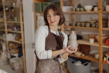 Smiling entrepreneur crafts woman holding mug in pottery studio while looking at camera 