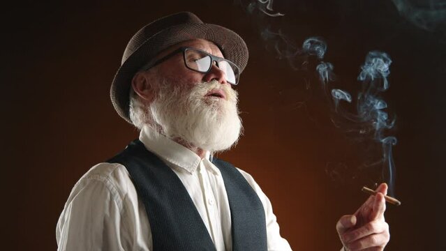 This distinguished senior gentleman sports a stylish fedora and glasses while smoking a cigar, his white beard adding to his wise and cultured appearance, set against a dark background. Camera 8K RAW 