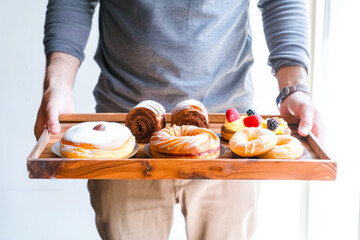 Cropped image of man holding wooden tray with fresh pastries and cakes.