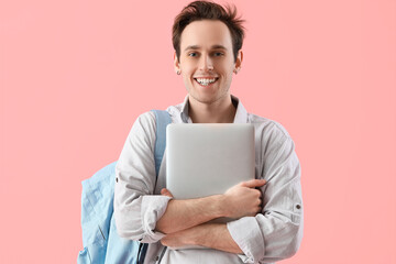 Male student with laptop on pink background