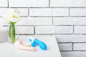 Vase with flowers, vibrators and tissue box on table near white brick wall