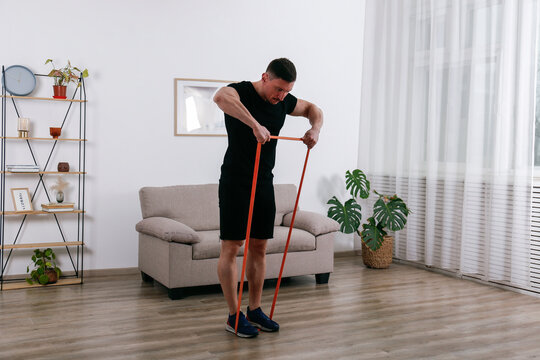 Bodybuilder doing shoulder exercises with the resistance fitness band at home. Copy space, interior background.
