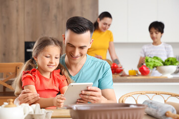 Little girl with her father using tablet computer in kitchen