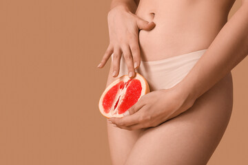 Young woman in panties with half of grapefruit on beige background, closeup. Sex concept