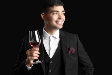 Young sommelier with glass of pink wine on black background