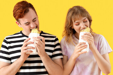 Young couple eating tasty sandwich wraps on yellow background