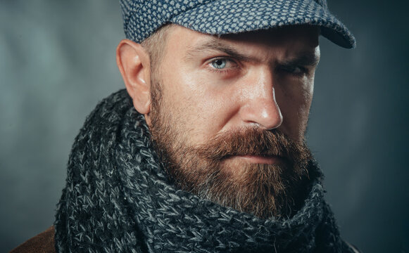 Winter knitwear. Closeup portrait stylish bearded man in gray cap and scarf. Fashion male model in winter outfit. Men fashion. Fashionable handsome man with beard and mustache in demi-season clothes.