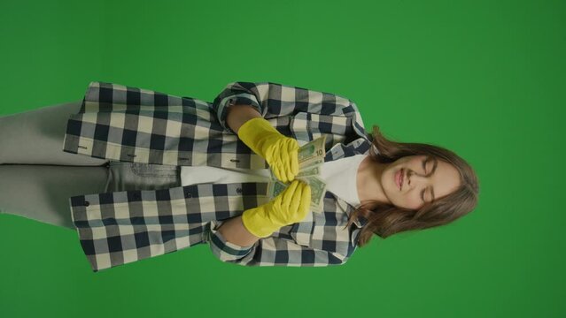 Vertical View.Green Screen. A Smiling Young Woman Housewife in Yellow Protective Rubber Gloves Counts Money in Dollars US. Efficient Work-from-home Setups.