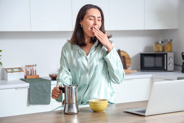 Pretty young woman with geyser coffee maker and cup of espresso yawning in modern kitchen