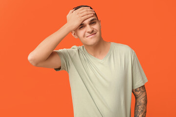 Handsome ashamed young man covering face with hand on orange background