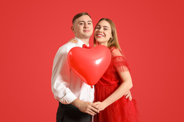 Fototapeta na wymiar Happy young couple with heart-shaped balloon on red background. Valentine's Day celebration
