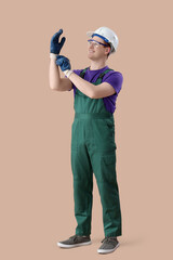 Male electrician putting gloves on brown background