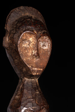 An African male figure portrait carved in wood isolated on black. Traditional African art with balanced shapes and volumes and beautiful black patina and kaolin pigments.