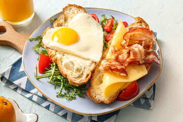 Plate with tasty fried egg, cut croissant, bacon, tomatoes and arugula on light background, closeup