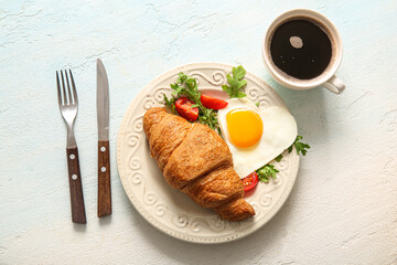 Plate with tasty fried egg, croissant, cup of coffee and cutlery on light background