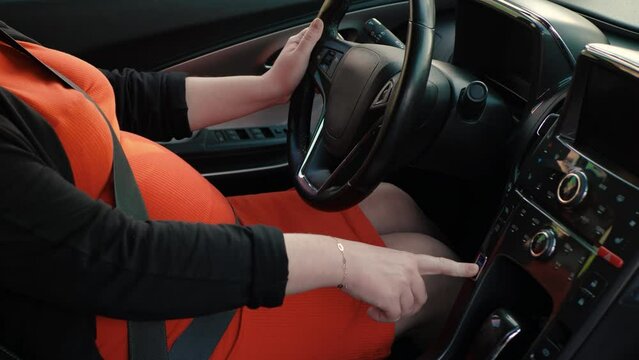Unrecognizable pregnant woman starting electric car, power button in car, modern expectant mother