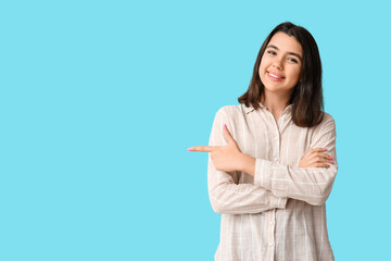 Young happy smiling woman pointing at something on blue background