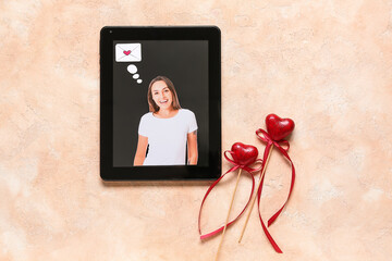 Tablet computer with photo of beautiful woman and heart shaped decor on beige grunge background. Concept of online dating