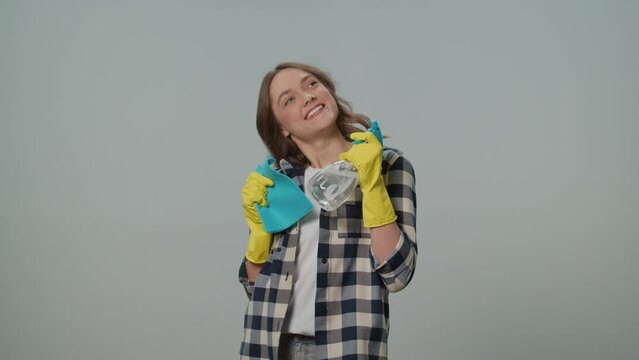 A Portrait of a Smiling Young Woman in Yellow Gloves,Holding a Cleaning Spray Bottle and Rag, Dancing on the Gray Background.A Female Housewife is Preparing to Clean. Decluttering Hacks.