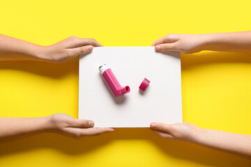 Child's hands with blank card and asthma inhaler on yellow background
