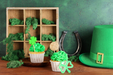 Tasty cupcakes with leprechaun hat, horseshoe and moss for St. Patrick's Day on wooden table against green grunge background