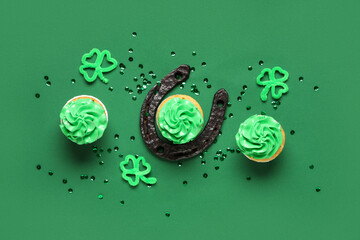 Tasty cupcakes with horseshoe, clovers and sequins for St. Patrick's Day on green background
