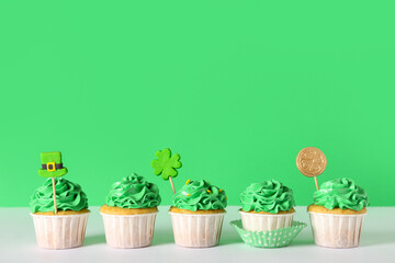 Tasty cupcakes for St. Patrick's Day on white table against green background