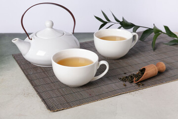 Bamboo mat with teapot, cups of tea and leaves on grunge table against white background