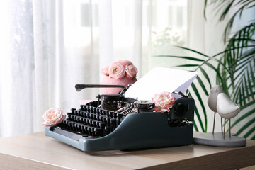 Vintage typewriter with paper sheet and roses on wooden table in room